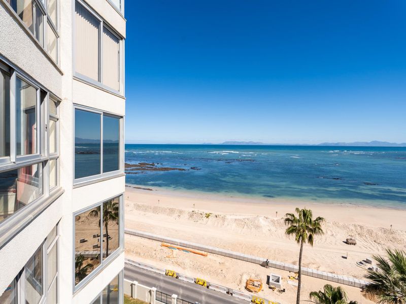 A high-angle view from an apartment window overlooking the coastline, sandy beach, and ocean horizon.
