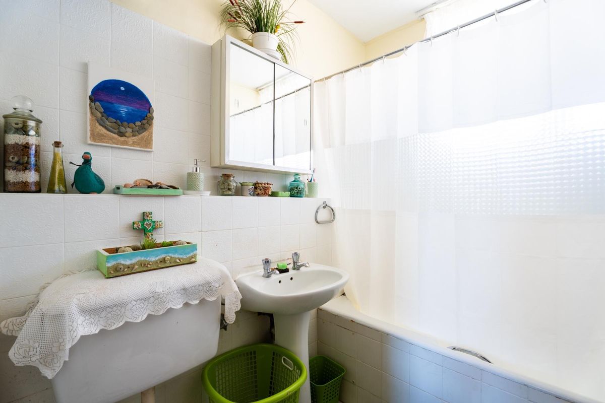 A functional bathroom featuring a pedestal sink, bathtub with shower curtain, and a mirrored medicine cabinet with tiled wall finishes.