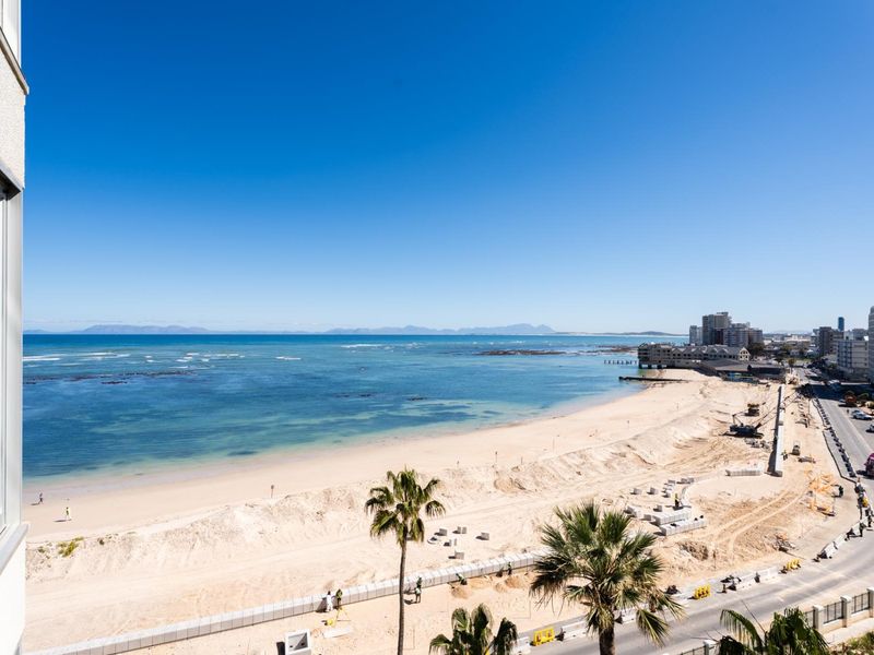 A panoramic coastal view overlooking the beach, ocean, and surrounding urban coastline from an elevated apartment perspective.