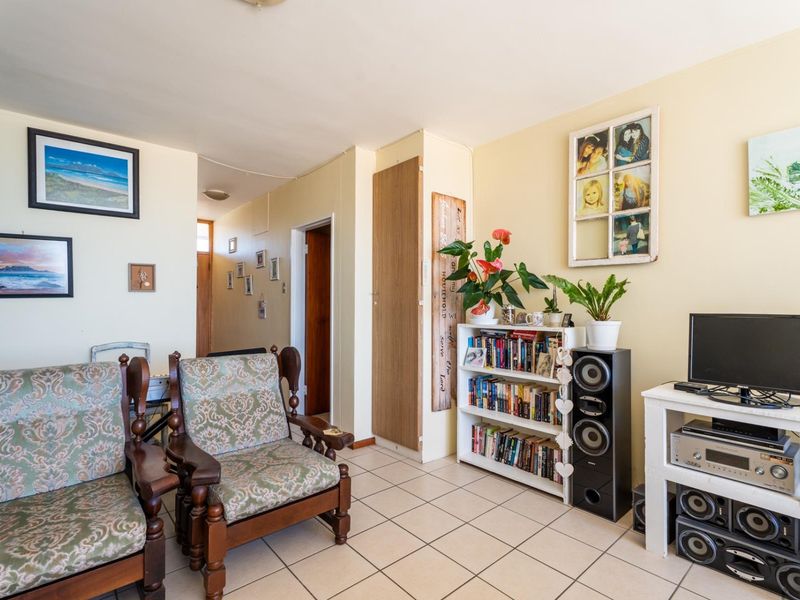 A living room area featuring tiled flooring and a built-in cupboard, providing access to the hallway and adjacent rooms.