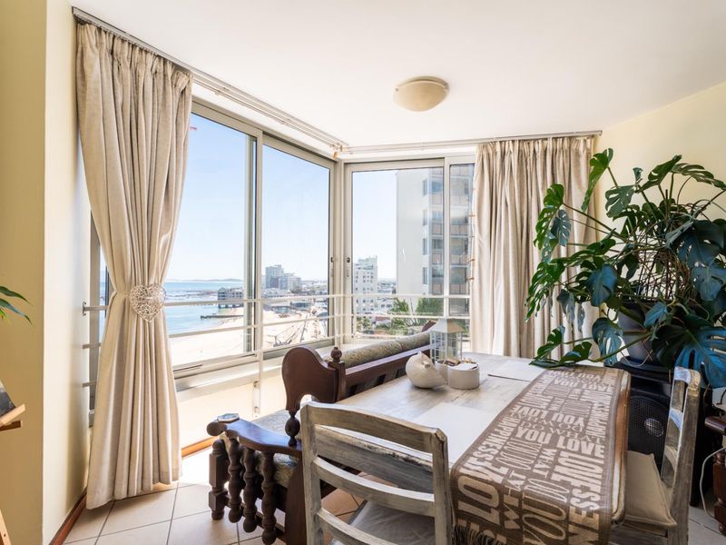 A bright living area featuring large sliding glass doors that offer expansive coastal and urban views, complemented by neutral tiled flooring.