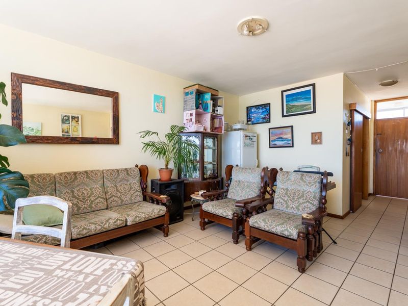 A living room area featuring ceramic floor tiles and neutral wall finishes, providing a functional space with direct access to the apartment hallway.