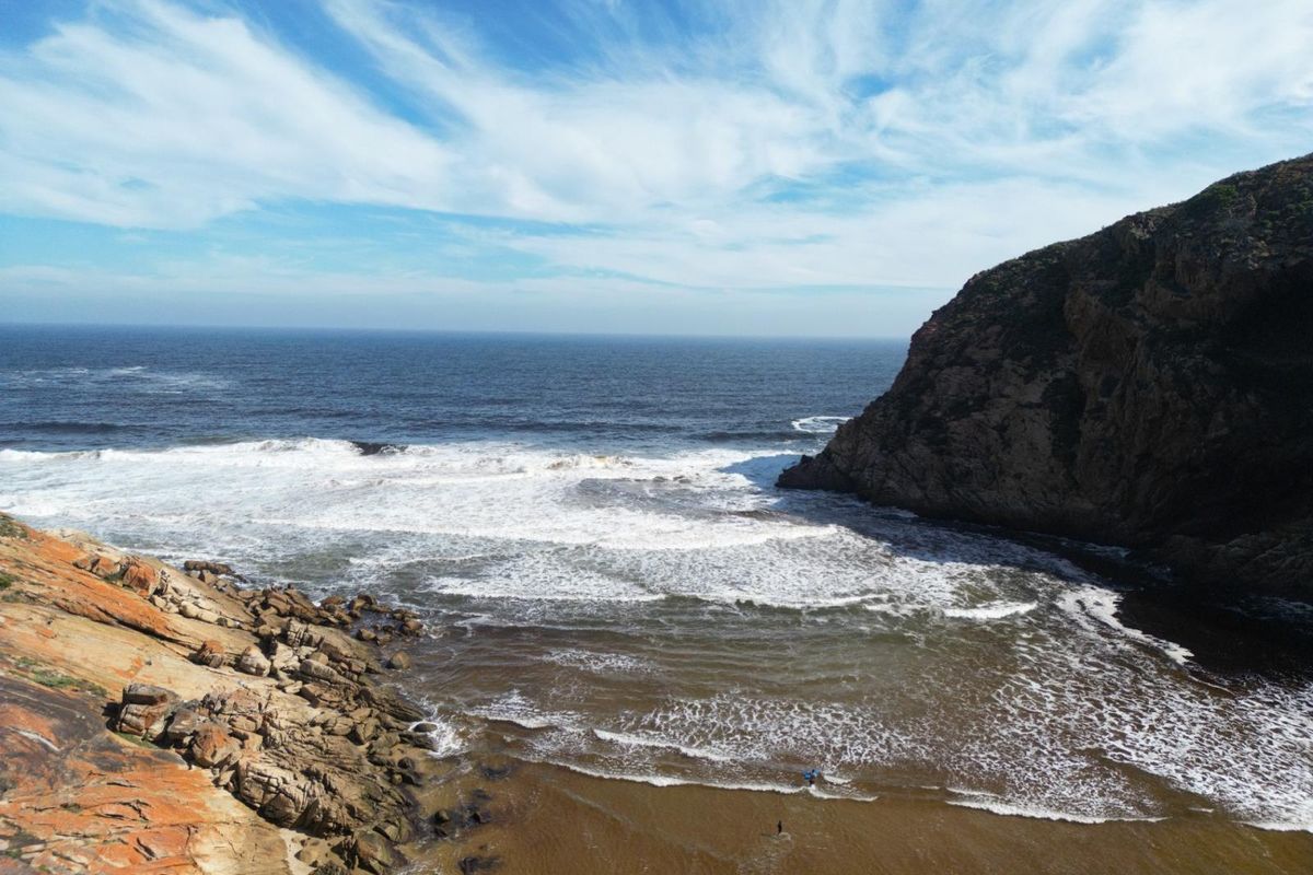 A scenic aerial view of a rugged coastal landscape featuring rocky cliffs, a sandy beach, and the ocean.