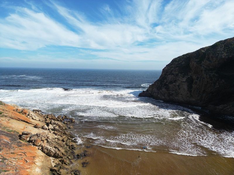A scenic aerial view of a rugged coastal landscape featuring rocky cliffs, a sandy beach, and the ocean.