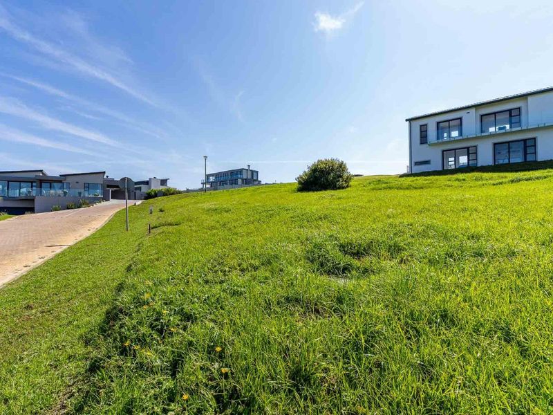 A view of a vacant residential plot featuring a grassy slope adjacent to a paved road in a modern estate setting.