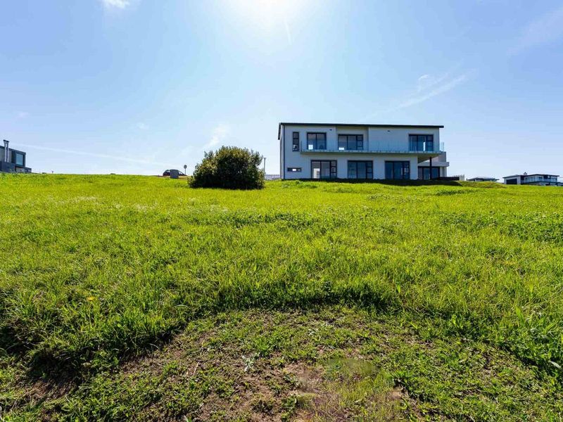 A view of a residential property situated on a sloped, grassy plot of land.
