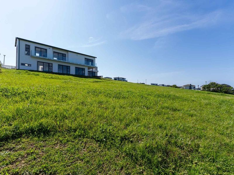 A view of a modern multi-story residential property situated on a sloped, grassy plot of land.