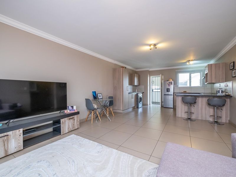 Spacious open-plan living area featuring tiled floors, a modern kitchen with built-in cabinetry, a breakfast island, and direct access to an exterior security gate.