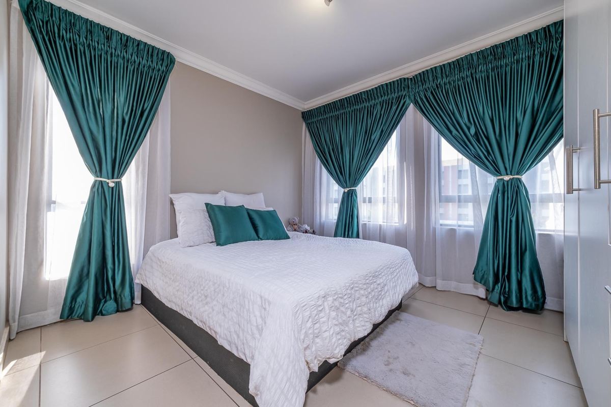 A well-maintained bedroom featuring neutral tiled flooring, crown molding, and a built-in wardrobe, complemented by large windows with elegant drapes.