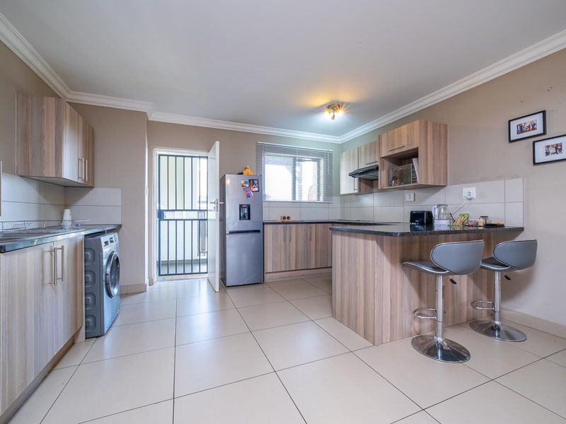 Modern kitchen featuring wood-finish cabinetry, granite countertops, a breakfast bar, and tiled flooring, with direct access to an outdoor area via a security gate.