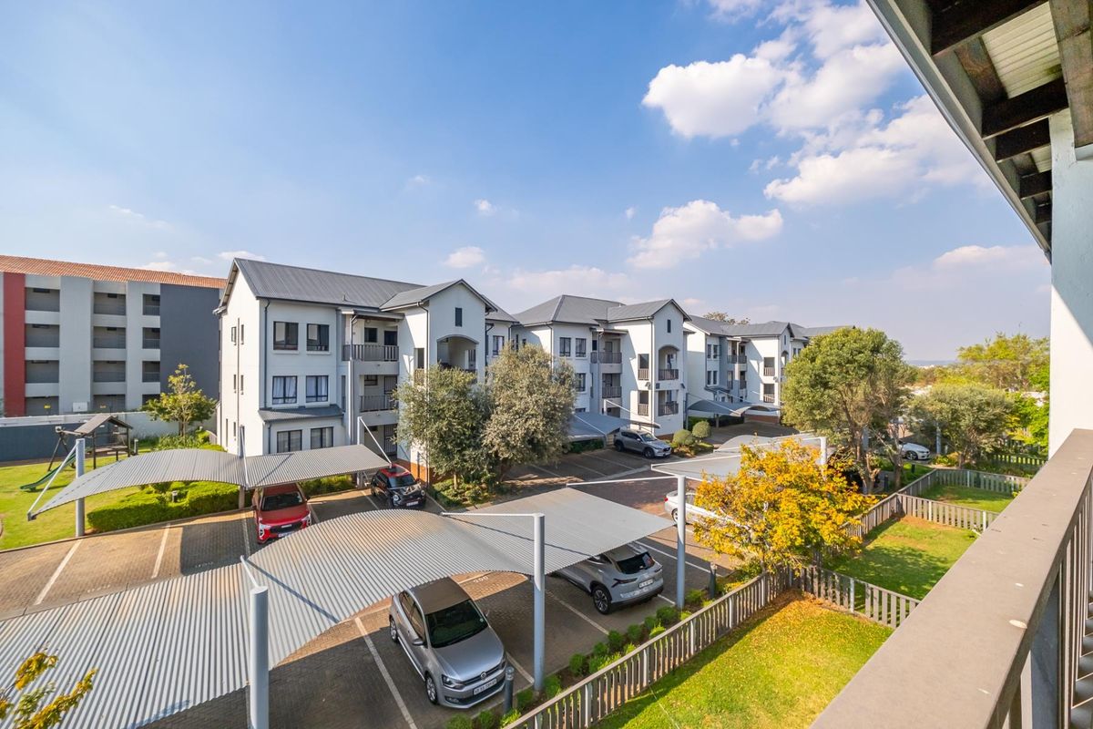 Elevated view of the apartment complex grounds, featuring covered parking bays, paved driveways, and well-maintained communal garden areas.