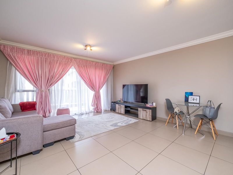 A bright and spacious living room featuring large format floor tiles, neutral wall tones, and a sliding glass door providing access to the balcony.