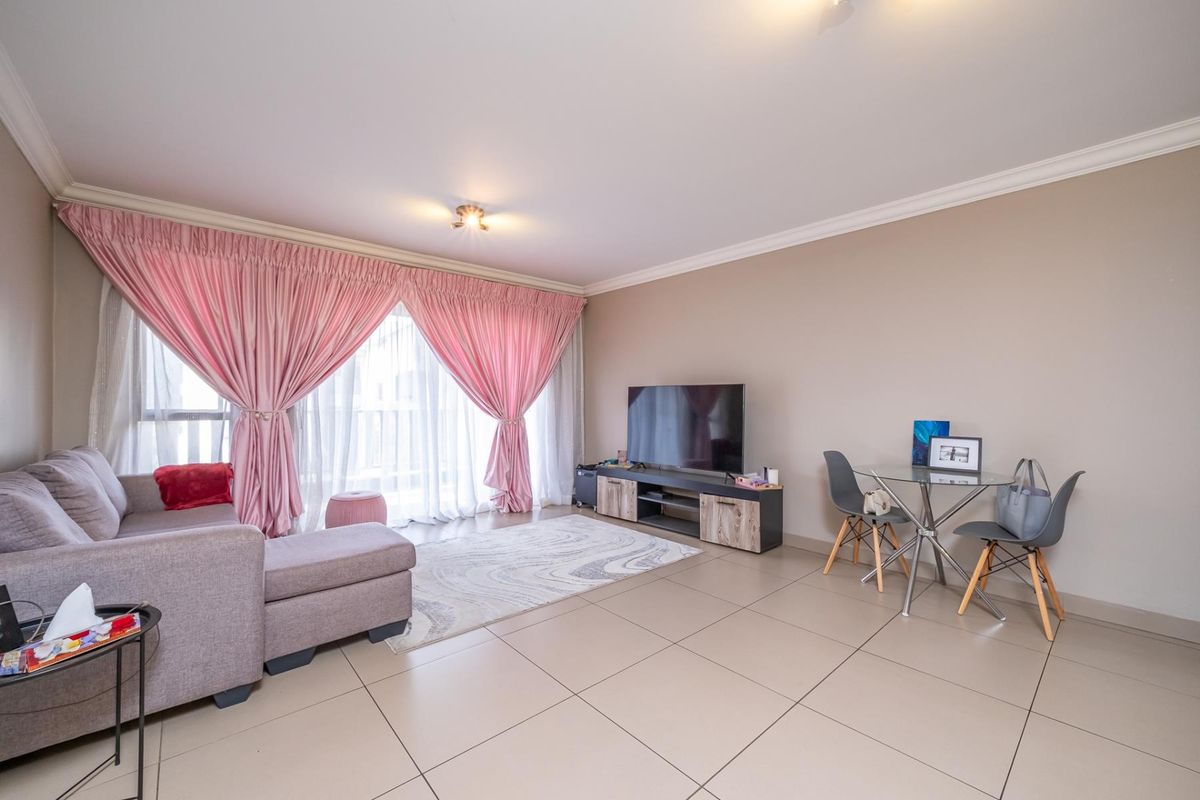 A bright and spacious living room featuring large format floor tiles, neutral wall tones, and a sliding glass door providing access to the balcony.