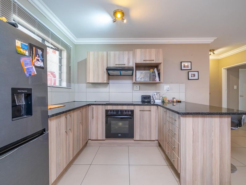 A functional kitchen featuring light wood-finish cabinetry, granite countertops, built-in oven, extractor fan, and tiled flooring with a clean, neutral aesthetic.