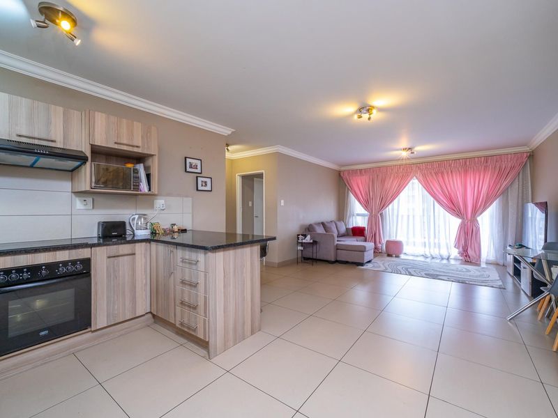 Spacious open-plan living area featuring a modern kitchen with granite countertops, built-in oven, and tiled flooring, leading to a bright lounge with balcony access.