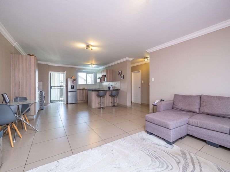 Spacious open-plan living area featuring tiled flooring, a modern kitchen with island, and direct access to an exterior security gate.
