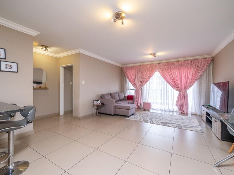 Spacious open-plan living area featuring neutral tiled flooring, coved cornicing, and a breakfast bar, with direct access to a balcony through sliding glass doors.