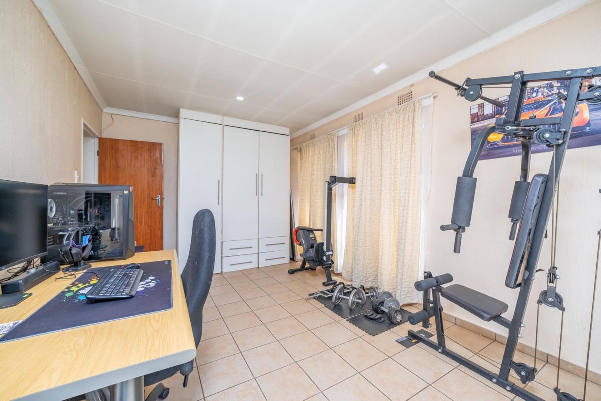 A multi-purpose bedroom featuring tiled flooring, built-in wardrobe storage, and recessed lighting, currently utilized as a home office and gym space.