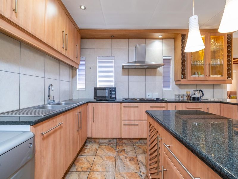 A well-maintained kitchen featuring light wood cabinetry, granite countertops, a central island, and a stainless steel extractor fan.
