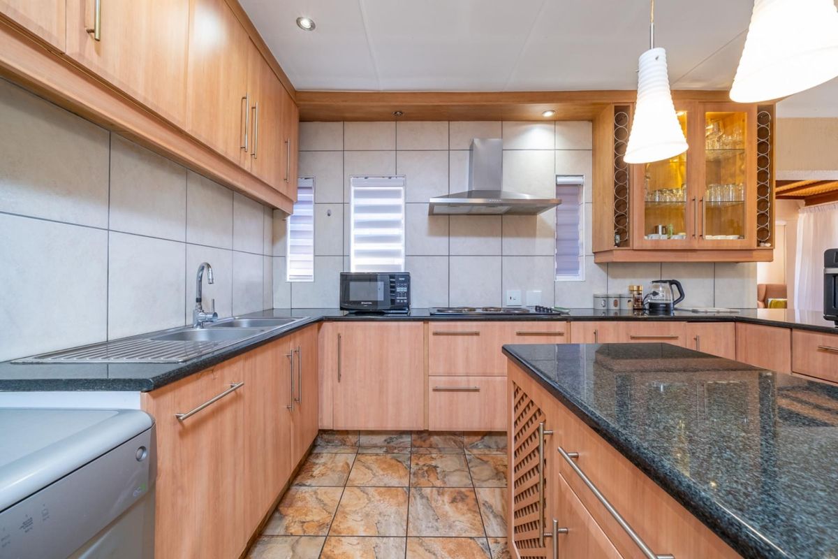 A well-maintained kitchen featuring light wood cabinetry, granite countertops, a central island, and a stainless steel extractor fan.