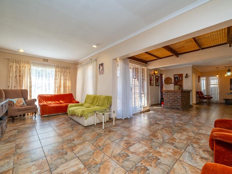 Spacious open-plan living area featuring tiled flooring, exposed timber beam ceilings, and a built-in brick bar counter, creating a versatile entertainment space.
