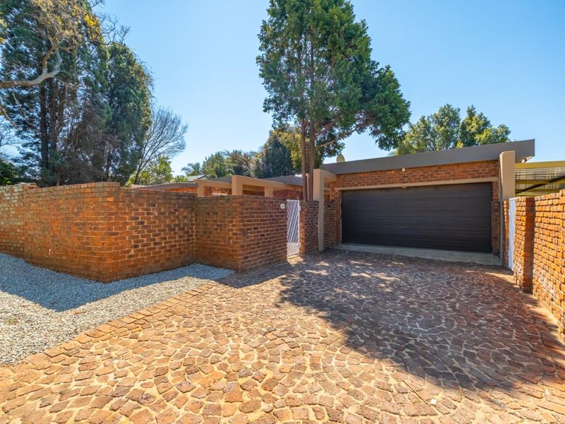 Front exterior view featuring a brick boundary wall, a cobblestone driveway, and a secure garage entrance.