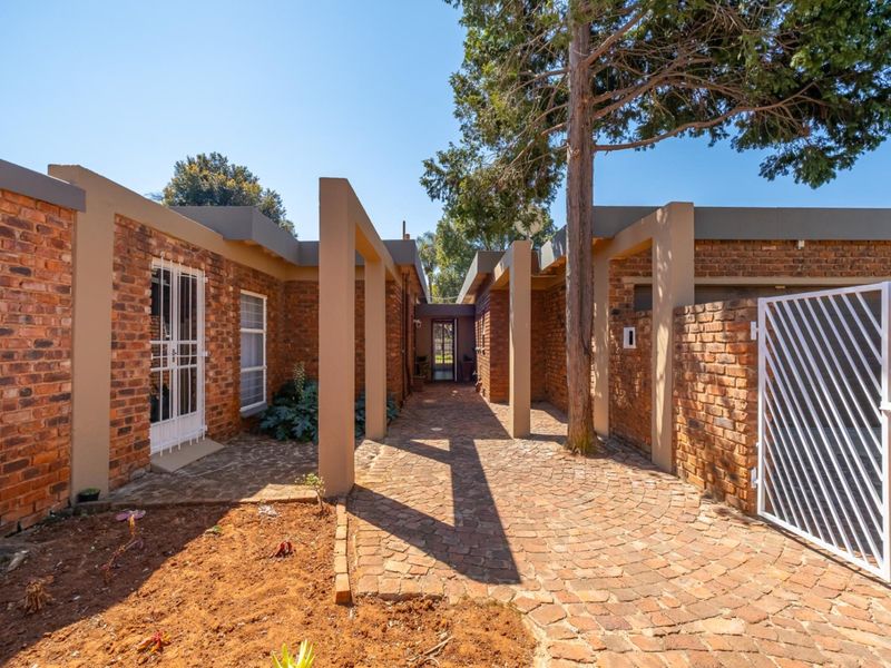 A well-maintained front entrance featuring a brick facade, cobblestone pathway, and secure gated access with established structural pillars.