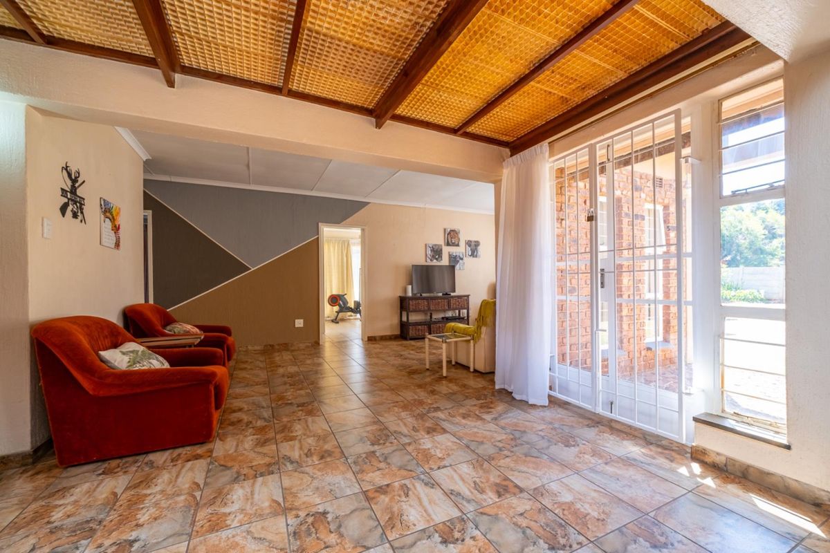 Spacious living area featuring tiled flooring, a unique exposed beam ceiling, and direct access to the exterior through a secure glass sliding door.