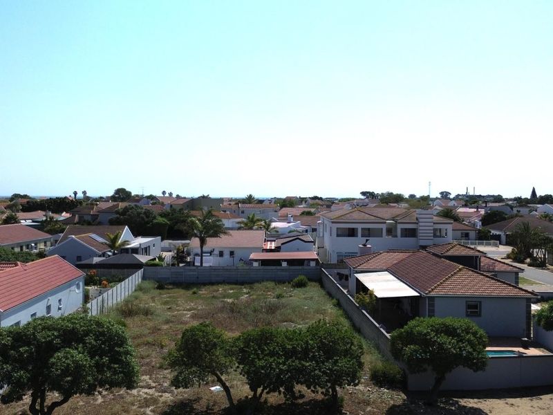 An aerial view of a vacant residential plot situated within an established suburban neighborhood, featuring boundary walls and surrounding residential properties.