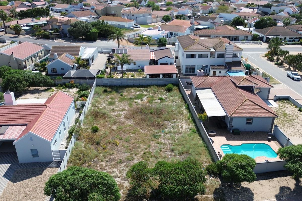 An aerial view of a vacant residential plot situated in a developed suburban neighborhood, surrounded by existing homes and boundary fencing.