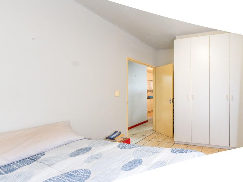 A bedroom featuring built-in cupboards and tiled flooring, with a doorway leading to an adjacent room.