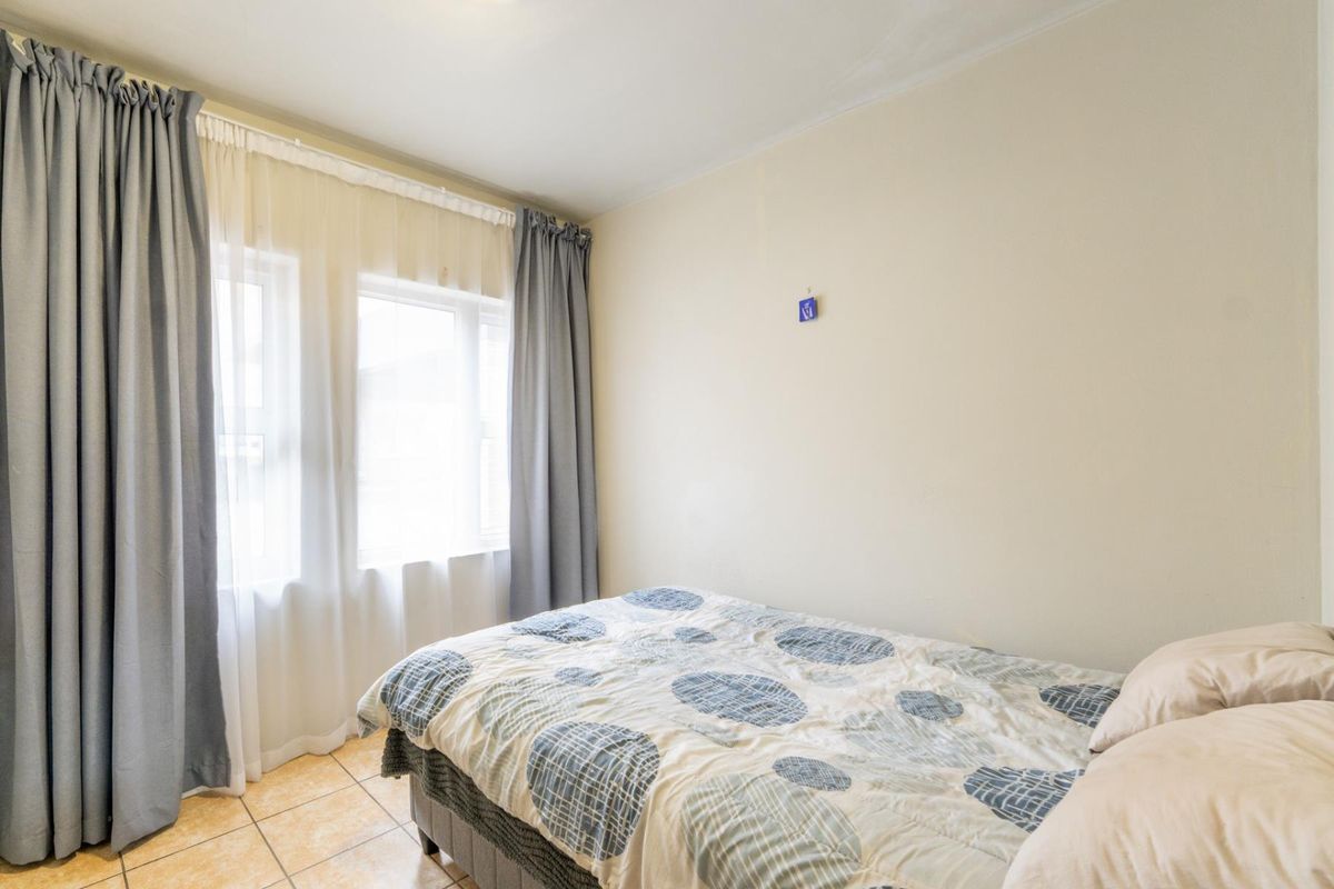 A functional bedroom featuring tiled flooring and large windows with installed curtain tracks, providing natural light to the space.