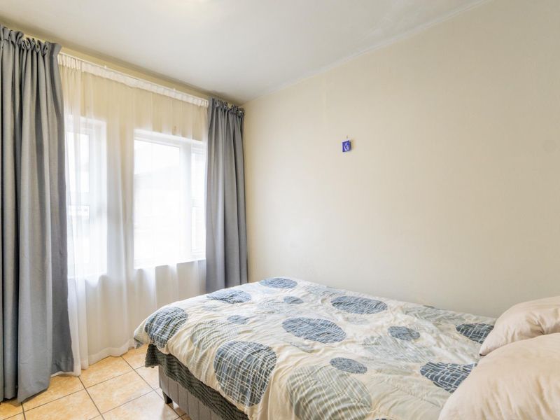 A functional bedroom featuring tiled flooring and large windows with installed curtain tracks, providing natural light to the space.