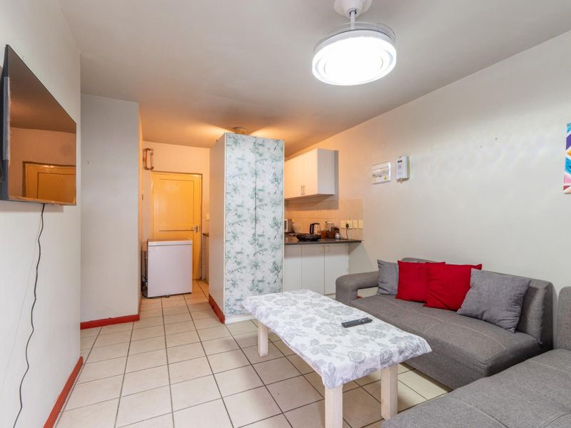 Open-plan living area featuring tiled flooring and a compact kitchenette with built-in cabinetry and laminate countertops.