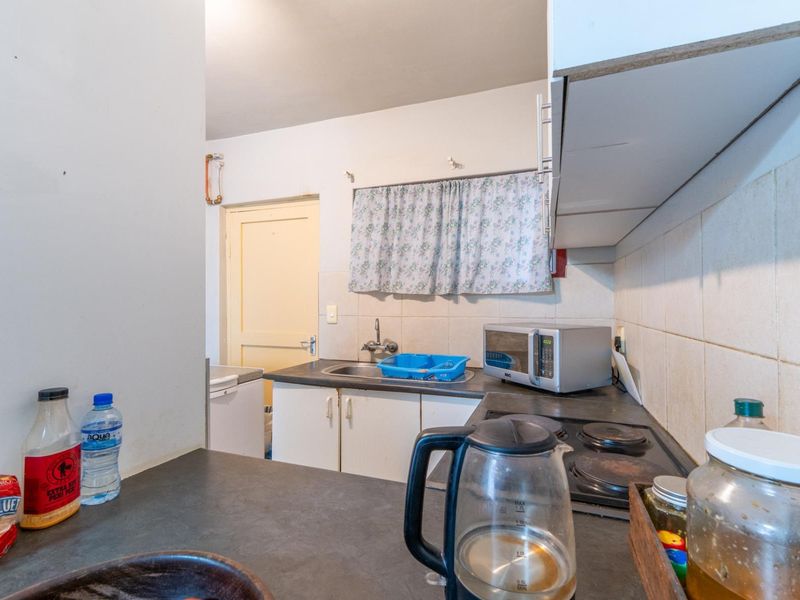 A compact kitchen featuring laminate countertops, a stainless steel sink, an electric hob, and tiled backsplash with dated cabinetry.