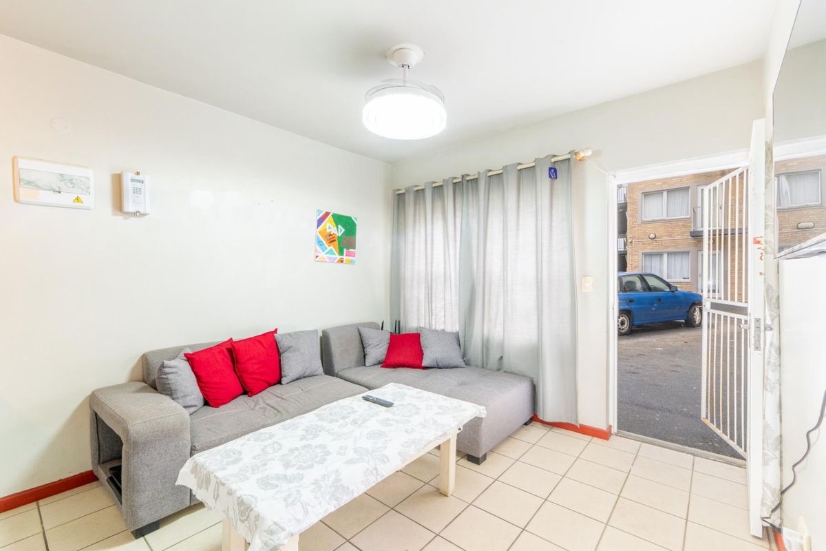 A functional living room featuring tiled flooring, a central ceiling light, and direct access to the exterior via a security gate.