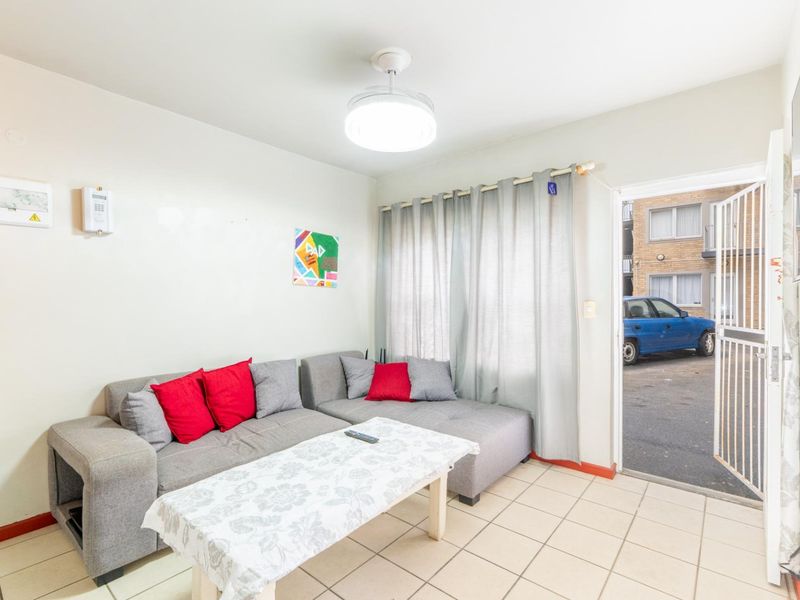 A functional living room featuring tiled flooring, a central ceiling light, and direct access to the exterior via a security gate.
