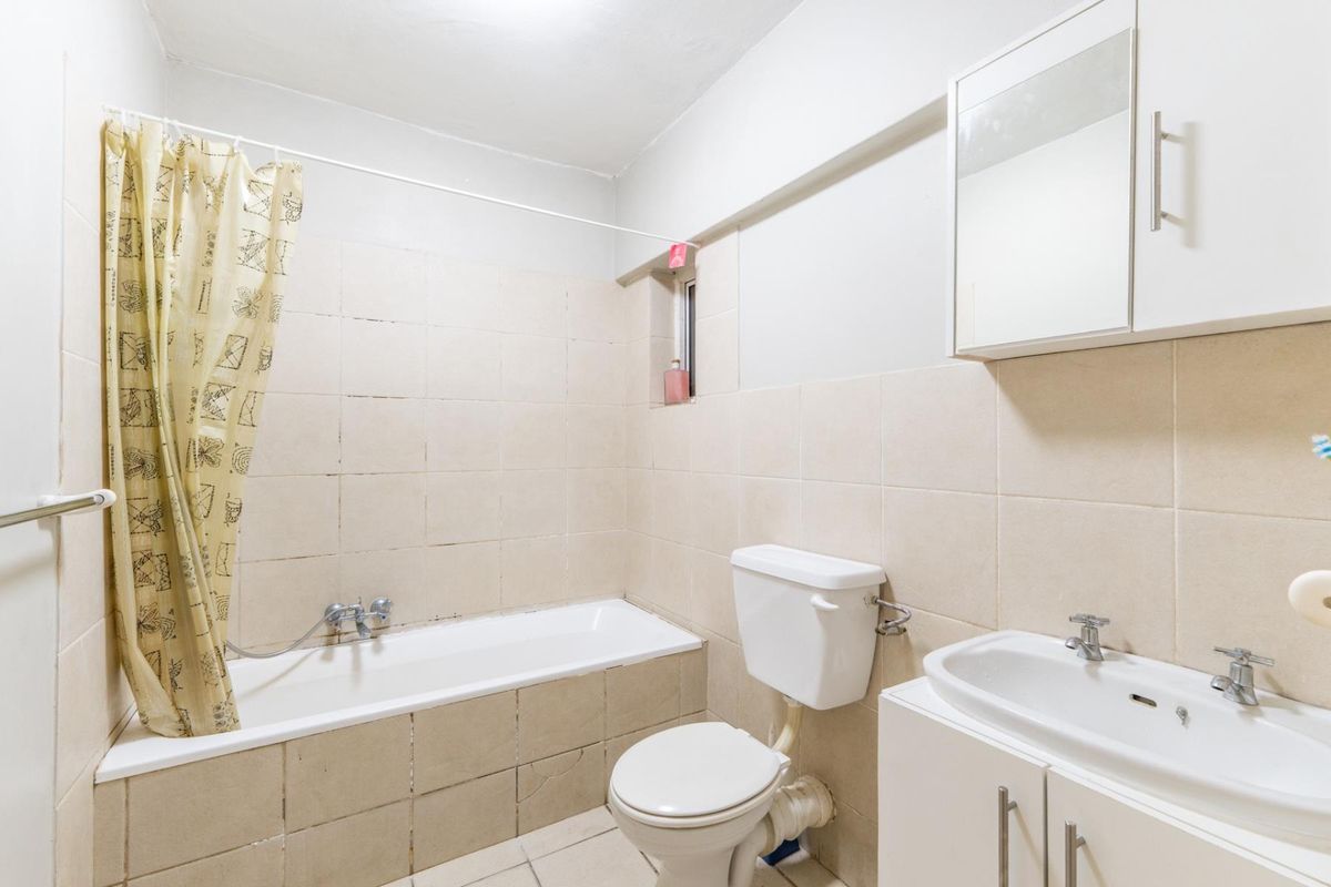 A functional bathroom featuring a bathtub with shower mixer, a standard toilet, and a vanity unit with a washbasin and wall-mounted cabinet.