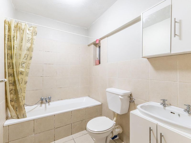 A functional bathroom featuring a bathtub with shower mixer, a standard toilet, and a vanity unit with a washbasin and wall-mounted cabinet.
