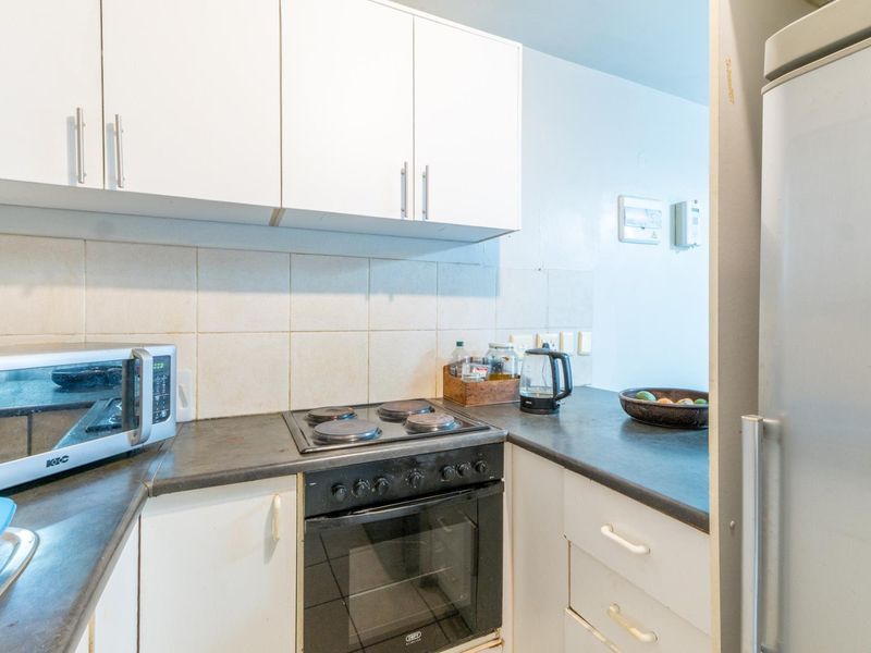 A compact kitchen featuring white cabinetry, dark laminate countertops, a tiled backsplash, and a built-in electric oven with a hob.