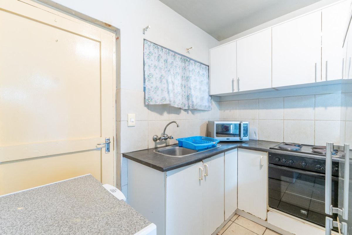 Compact kitchen featuring built-in cabinetry, a stainless steel sink, and an integrated oven with electric hob, finished with tiled backsplash and flooring.
