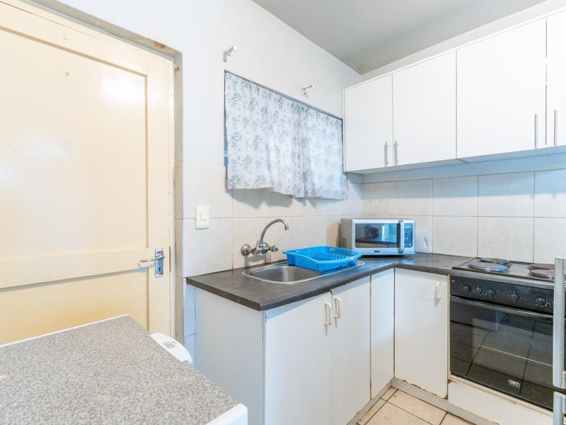 Compact kitchen featuring built-in cabinetry, a stainless steel sink, and an integrated oven with electric hob, finished with tiled backsplash and flooring.