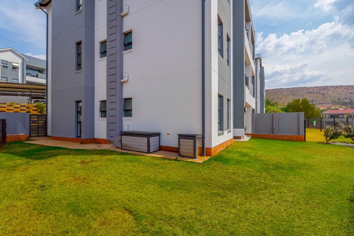 A view of the rear exterior of the apartment building, featuring a well-maintained lawn, paved walkway, and secure perimeter fencing.