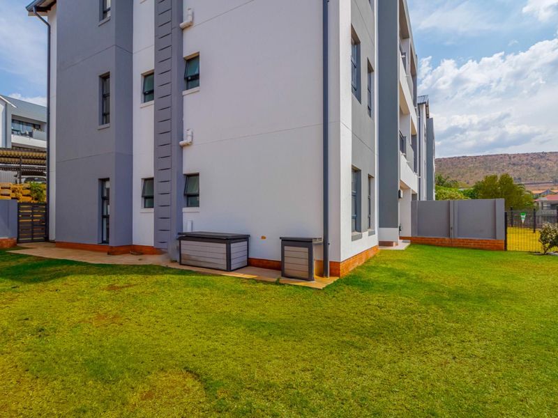 A view of the rear exterior of the apartment building, featuring a well-maintained lawn, paved walkway, and secure perimeter fencing.