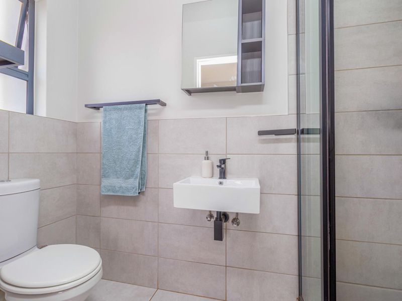 A modern, well-maintained bathroom featuring a wall-mounted basin, toilet, and a glass-enclosed shower with neutral wall and floor tiling.