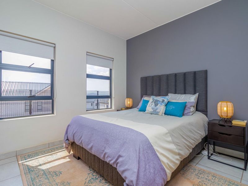 A well-maintained bedroom featuring tiled flooring, an accent wall, and large windows with roller blinds, providing ample natural light.