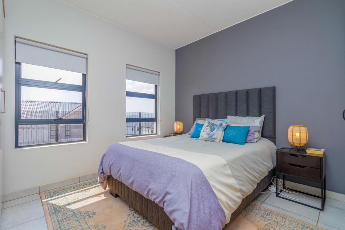 A well-maintained bedroom featuring tiled flooring, an accent wall, and large windows with roller blinds, providing ample natural light.