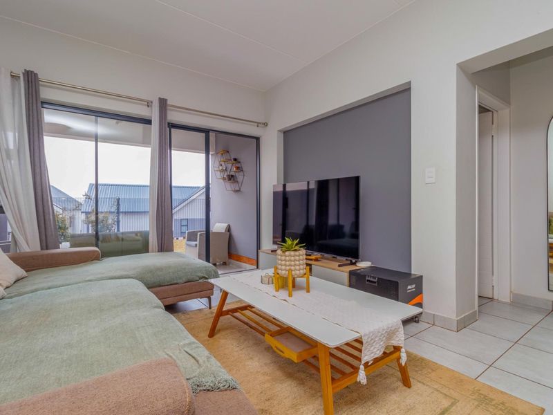 A bright living room featuring tiled flooring, a recessed feature wall, and large sliding glass doors providing access to an outdoor patio area.
