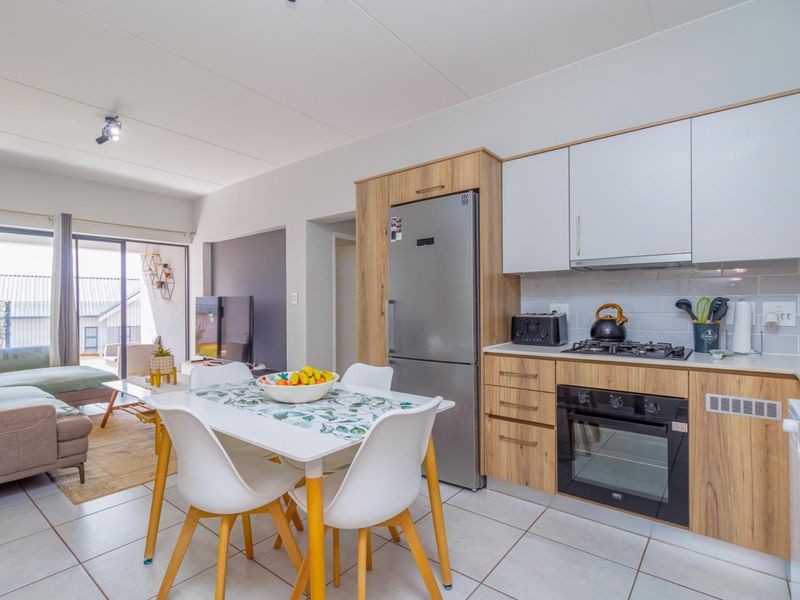 Open-plan living and kitchen area featuring modern wood-finish cabinetry, gas hob, electric oven, tiled flooring, and direct access to a balcony through sliding doors.