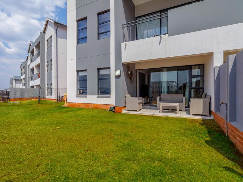 Rear view of the apartment building featuring a private garden, a paved patio area, and a balcony accessible via sliding glass doors.